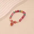 Detailed macro view of colorful tourmaline crystal bracelet with pink carved flower charm - Persimmon Good Fortune Style