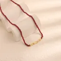 Primo piano di una collana di perline di granato rosso con accenti dorati su sfondo materico. - Granato Pezzi d'Oro