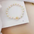 Close-up of white beaded bracelet with golden spacers and a central flower charm detail. - No. 3 Small Flower