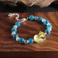 Nahaufnahme eines blauen Achat-Armbands mit einem gelben neunschwänzigen Katzenanhänger - Zitronengelber Liggende Katze Stil