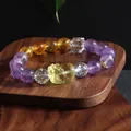Detail of amethyst and citrine beaded bracelet with a carved Pixiu charm on wooden stand - Pixiu / Purple and Yellow