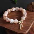 Detailed close-up of a natural crystal beaded bracelet with a golden bowknot charm. - Black Gold Super Seven Style / Black Gold Super Seven Bow