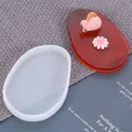 Molde de silicona blanco para posavasos junto a una pieza de resina ámbar acabada. - Óvalo Irregular (60-229) / 1 Pieza