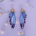 Detaillierte Nahaufnahme von blauen Schmetterlingsflügel-Ohrringen mit Strasssteinen - Farbverlauf Blau-Gold-Strass
