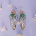 Nahaufnahme von Zikadenflügel-Ohrringen mit grünem Farbverlauf und Kristallen - Roségold Strass Zikadenflügel Stil / Grün