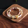 Detail shot of multi-layered natural crystal bead bracelet with golden charm on wood tray - Red Ghost and Yellow Crystal Mix Style