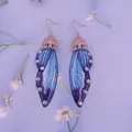 Makro-Detail blauer Schmetterlingsflügel-Ohrringe mit Strasssteinen auf Blumen. - Farbverlauf Blau-Roségold-Strass