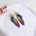 Makroansicht von Ohrringen aus Zikadenflügeln mit schillernden Strasssteinen und Filigran - Gold - Mehrfarbiger Lila Strass