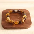 Detailed view of natural tiger eye and yellow crystal beaded bracelet on a wooden stand. - Citrine Style / 12mm Ball