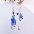 Elegante asymmetrische blaue Schmetterlingsflügel-Ohrringe mit lila Perlen und Goldkette - Blauer Strass-Gold