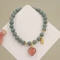 Primer plano de una pulsera de cuentas de jade con un colgante de corazón de cuarzo fresa - Colgante Corazón de Cuarzo Fresa / Gris Azulado