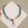 Primo piano di un elegante bracciale di perle di giada verde con perla e ciondolo a ciambella - Jadeite Pingan Buckle Pendant / grigio bluastro