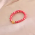 Nahaufnahme eines rosa Kristallarmbands mit Kürbis-Anhänger auf edler Seide liegend. - Rosa Hellorange Kürbisform Stil
