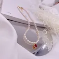 Detailaufnahme einer zweireihigen Reisperlenkette mit rotem Zirkon-Anhänger - Roter Strass-Tropfen-Stil / Gold