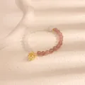Primo piano di un braccialetto di perline con pietre rosa e bianche e un ciondolo a lanterna. - Casa dorata