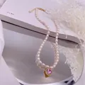 Detailaufnahme einer Süßwasser-Reisperlenkette mit funkelndem rosa Zirkonia-Herzanhänger. - Rosa Strass-Herz-Stil / Gold