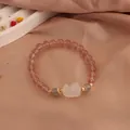 Detail view of strawberry crystal bracelet with a moonstone cat claw charm on pink fabric - Fox Style