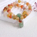 Nahaufnahme eines natürlichen Jinsiyu-Perlenarmbands mit Maiglöckchen-Anhängern - Doppellagiges Armband Aus Goldener Seide Und Jade Mit Maiglöckchenmotiv