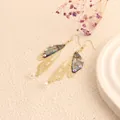 Detailed view of long cicada wing earrings with gold hollow frames and iridescent accents - Gold Frame / Light Blue Landscape
