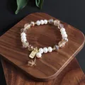 Detailansicht eines Süßwasserperlenarmbands mit Kristallen und Good-Luck-Anhänger. - Süßwasserperle Kristall Glücksbringer Stil