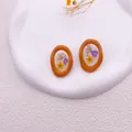 Détail macro de boucles d'oreilles oranges avec de vraies fleurs séchées violettes et jaunes - Ovale irrégulier / Orange