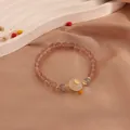 Detailed close-up of a strawberry quartz and moonstone bracelet with a gold coin charm - White Jade Style