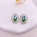 Detalle de pendientes ovalados de resina con flores secas azules y copos de pan de oro - Azul