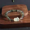 Detail shot of a green phantom crystal bracelet with a cute yellow fox charm on dark wood - Lying Cat Style