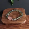 Macro detail of green phantom crystal bracelet with pink carved lion mascot on wood - Pi Xiu Style 2 (Strawberry Quartz)