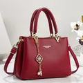 Vista dettagliata di un'elegante borsa a mano in pelle bordeaux con dettagli dorati e ciondolo - 26*11*18 / Rosso