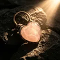 Gros plan d'un pendentif cœur en quartz rose bohème avec finition bronze sur des rochers - En Forme de Cœur / Quartz rose