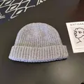 Close-up of a grey ribbed knit beanie hat on a dark surface with an artistic prop card - Approx. 56-58cm (Elastic) / Round Cuffed Landlord Hat / Light Heather Grey