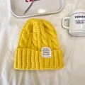 Primo piano di un berretto giallo a maglia a trecce con etichetta decorativa bianca - 55-59cm / Giallo