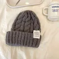 Primo piano di un berretto grigio a maglia treccia con etichetta retro in atmosfera accogliente - 55-59cm / Grigio