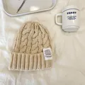 Dettaglio ravvicinato di un morbido berretto beige in maglia a trecce con etichetta vintage - 55-59cm / Beige