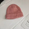 Close-up view of a pink ribbed knitted beanie cap on a white textured fabric background - One Size / Pink