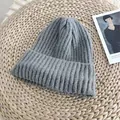 Macro detail of a grey ribbed knit beanie hat lying on a natural woven straw mat. - 54-58cm / Gray