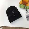Dettaglio di un berretto hip-hop nero con una spilla da balia d'argento su un tavolo bianco. - 55-58cm (Elastico) / Stile Spilla Singola