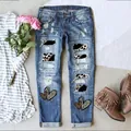 Detailansicht der verwaschenen blauen Jeans mit Leoparden-Patches und Herz-Grafik-Akzenten - S / Unterteile / Blau mit Leopardenherz-Druck