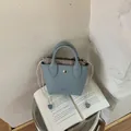 Hellblaue Mini-Handtasche aus Leder mit gestreiftem Innenfutter auf einer Buchseite - Mini / Blau