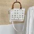 Close-up of white patent leather bucket bag with bamboo handle and floral beadwork - White