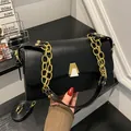 Détail d'un sac carré en cuir noir avec une bandoulière en chaîne dorée et fermoir en métal - Noir