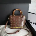 Brown patent leather shoulder bag featuring a vintage bamboo handle and gold flower details - Brown