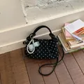 Korean style black polka dot handbag with elegant pearl bow charm on wooden floor. - Black