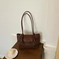 Elegante braune geflochtene Unterarm-Tasche auf einem antiken Holztisch platziert. - Braun
