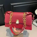 Détail d'un sac carré rouge avec une bandoulière chaîne dorée et un fermoir métallique. - Rouge