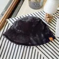 Close-up of black faux fur bucket hat with soft plush texture on striped background - Black