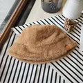 Detailed close-up of a brown plush faux fur winter bucket hat on striped fabric - Camel