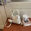 Cream leather Boston bag with cute bear charm displayed on a desk with coffee and books - With Bear Charm / Off White