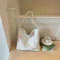Elegant white hobo bag with floral embroidery and twisted rope handle on a wooden desk - Off White